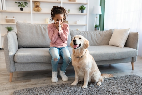 African American girl sneezing and holding tissue next to her dog