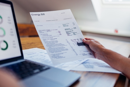 A person reviews their energy bill while using a laptop at home.